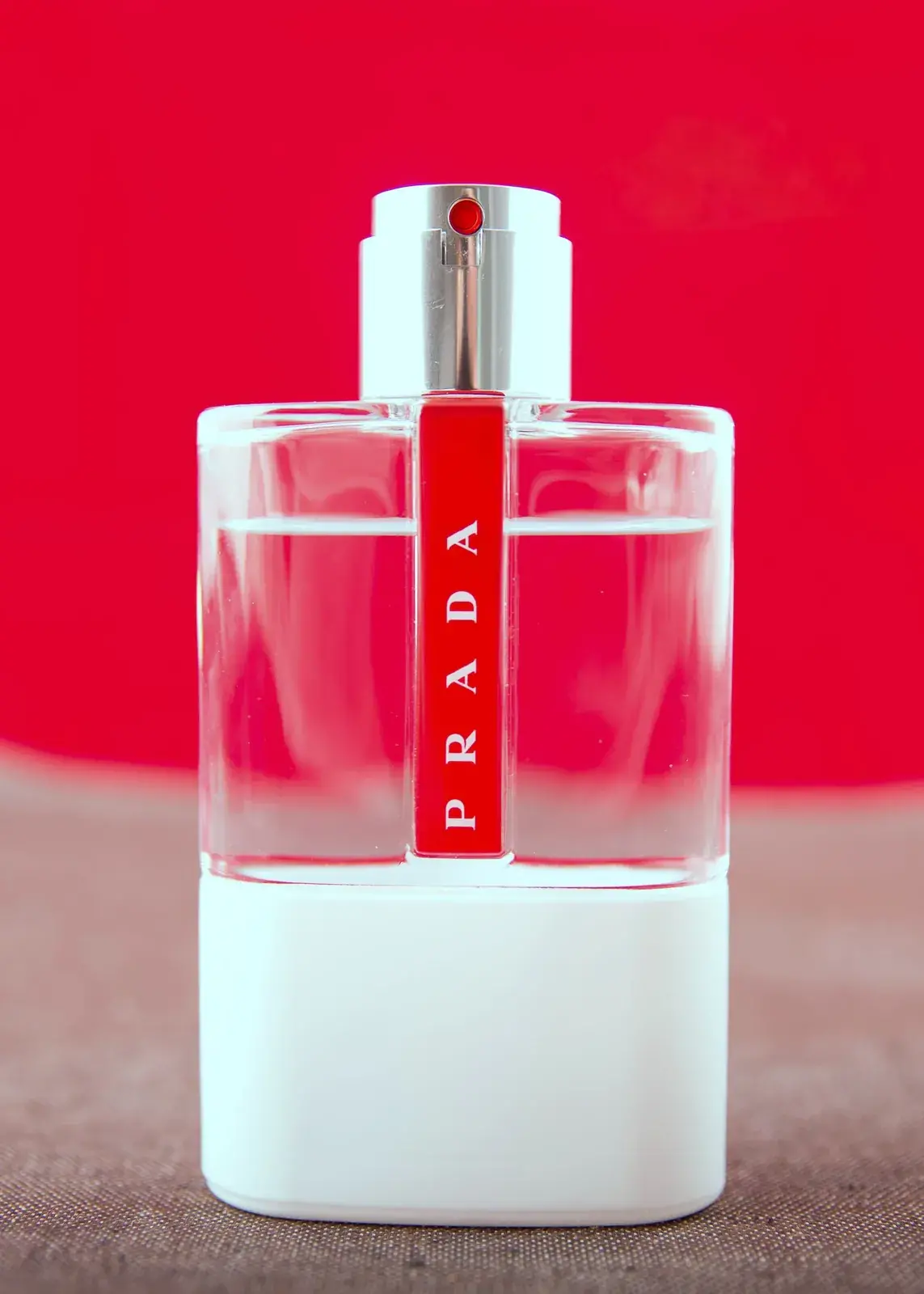 Photographie de produit haut de gamme d’un flacon de parfum sur fond rouge, mettant en valeur le verre, la transparence et la finition